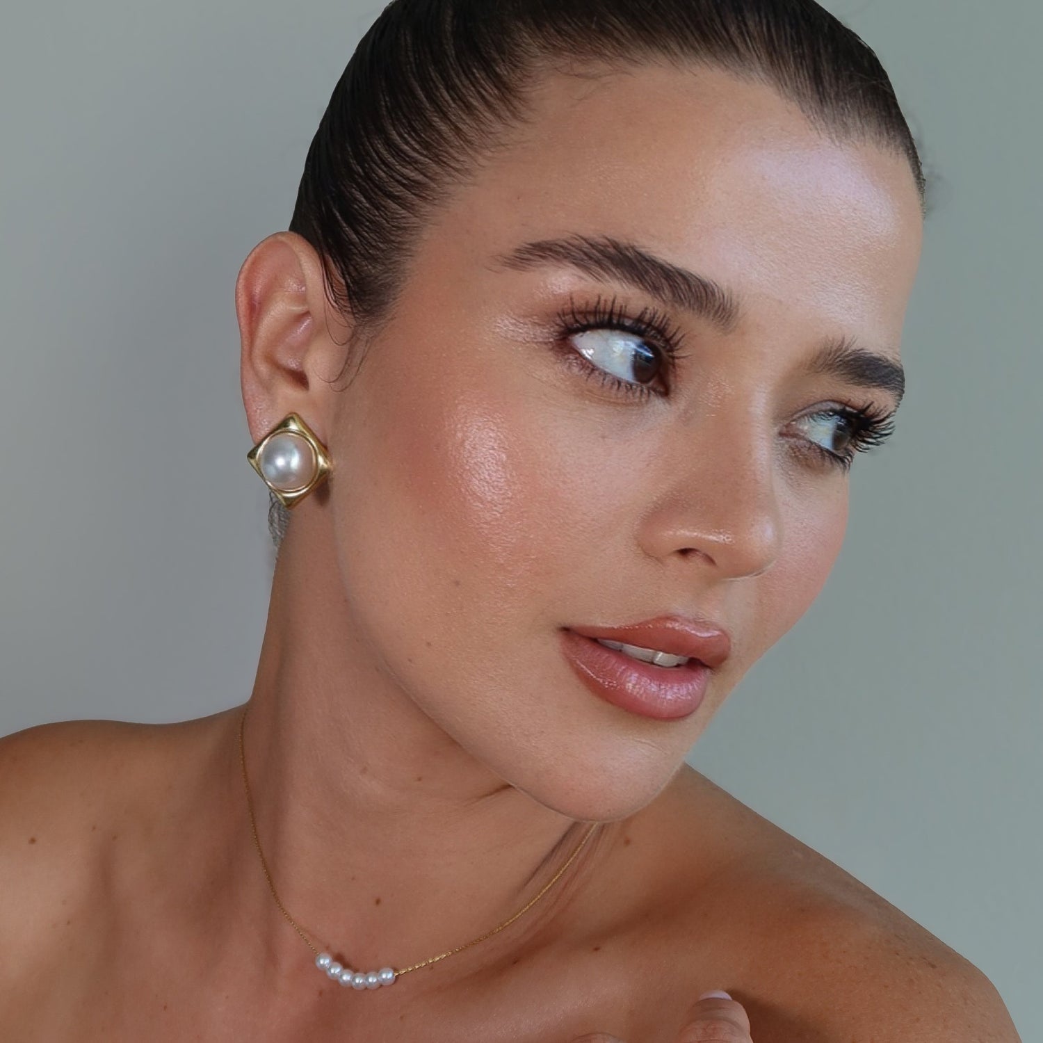 Woman wearing gold earrings and a ring with a plain background