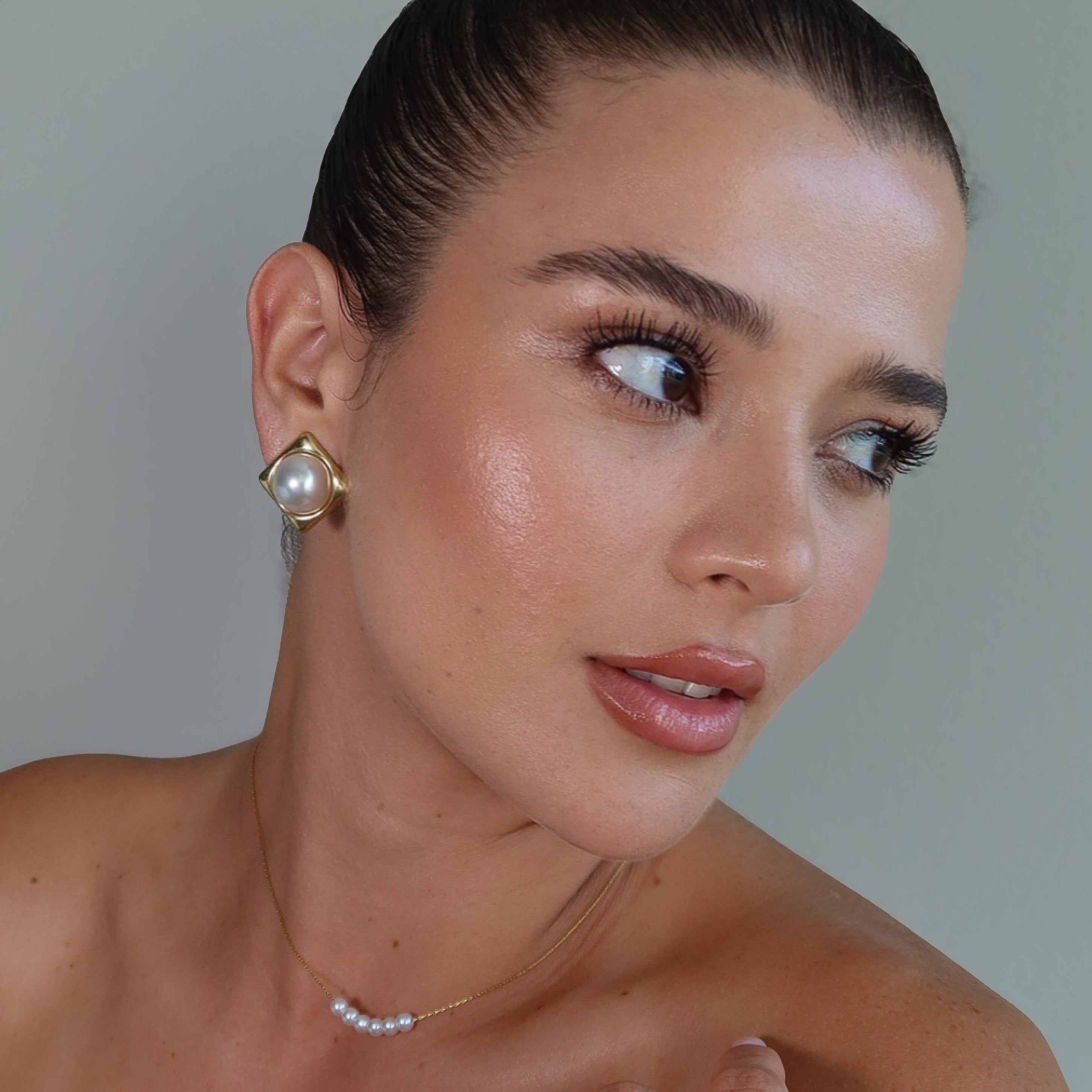 Woman wearing gold earrings and a ring with a plain background