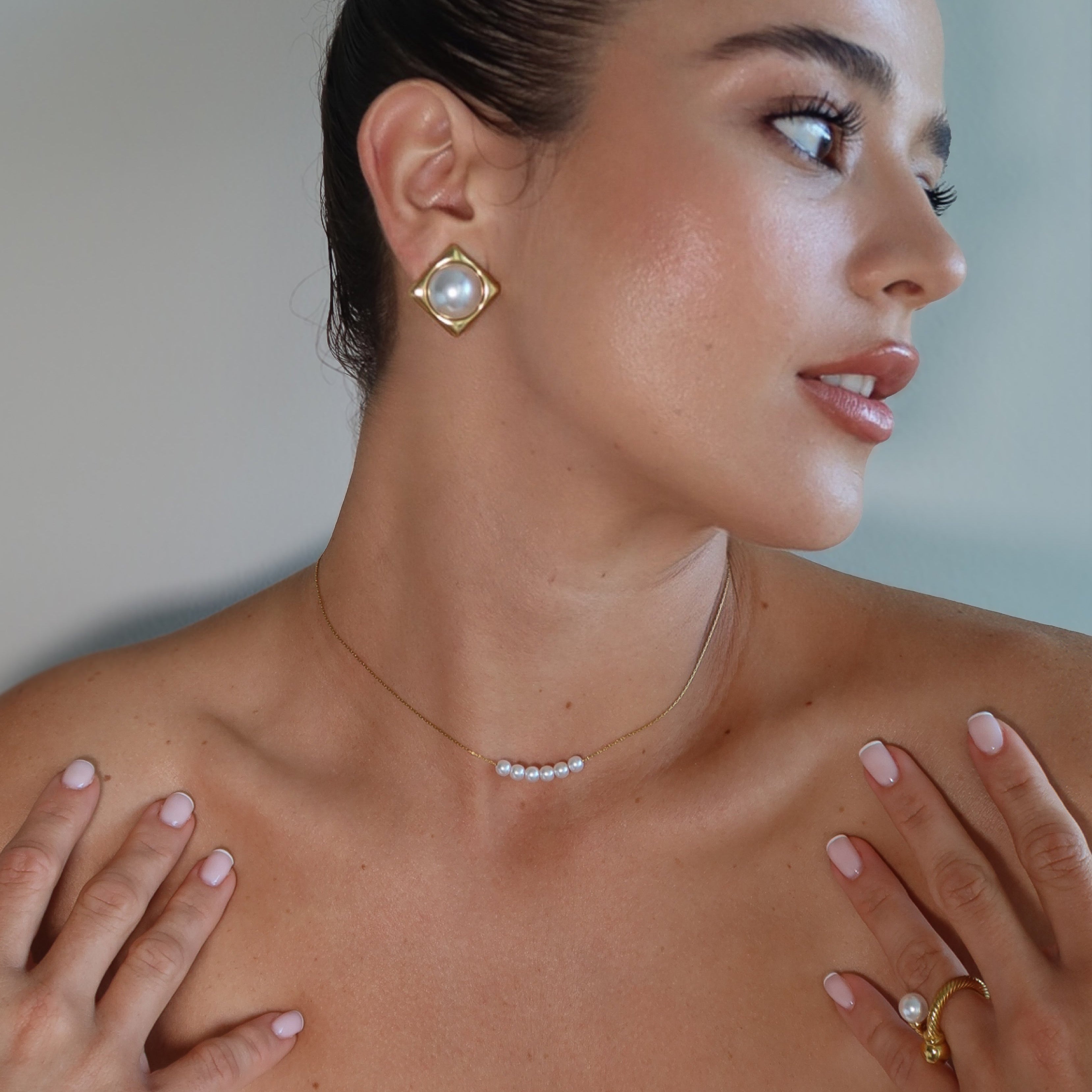 Woman wearing gold earrings, necklace, and ring with a plain background
