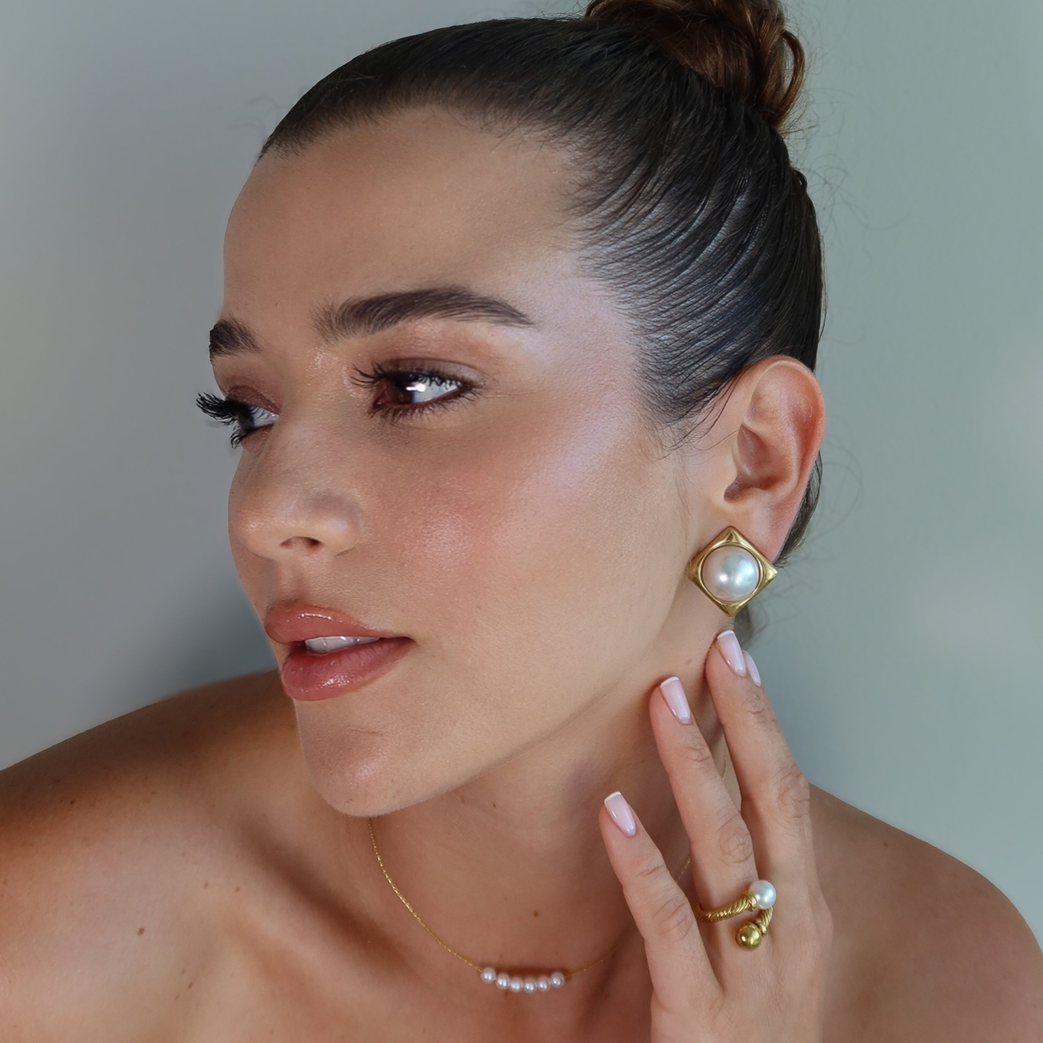 Woman wearing gold plated earrings CLAM and the waterproof gold plated ring SOLARA against a neutral background