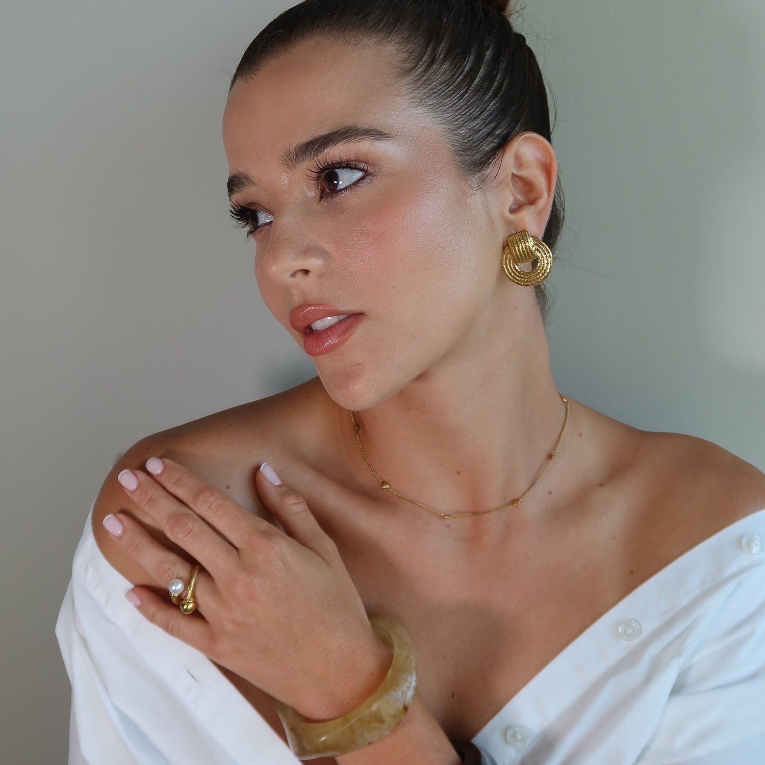 Woman wearing gold plated earrings JOY and the waterproof gold plated ring SOLARA against a neutral background