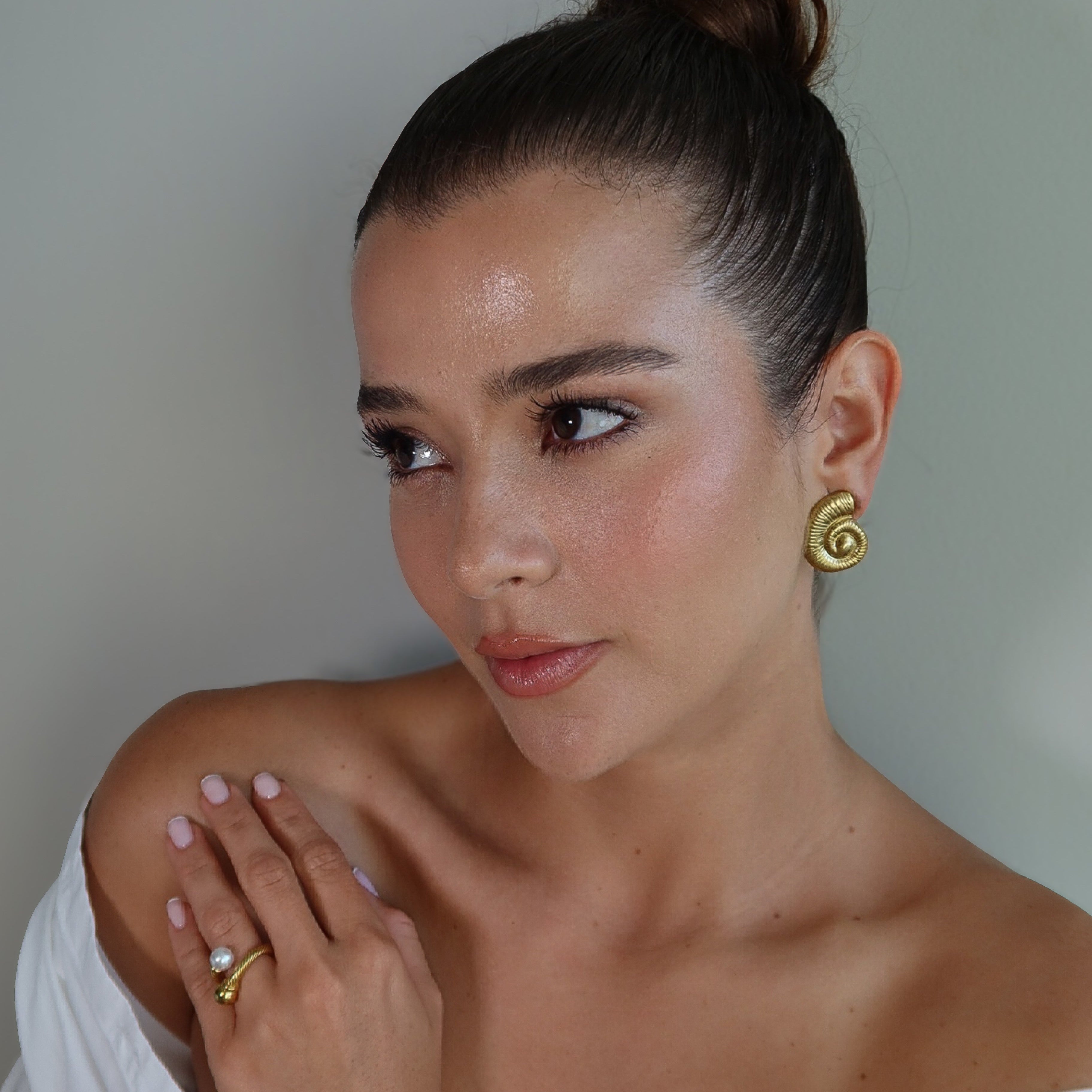 Woman wearing gold plated earrings SEASHELL and the waterproof gold plated ring SOLARA against a neutral background