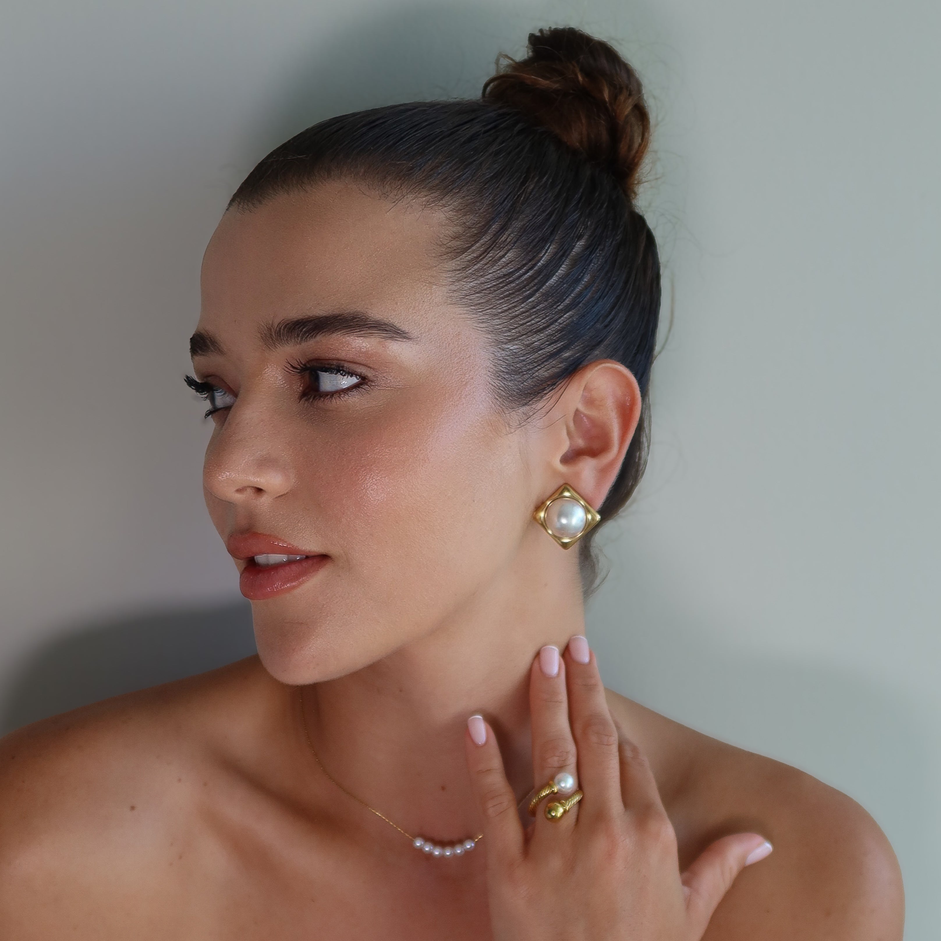 Woman wearing gold plated earrings CLAM and the waterproof gold plated ring SOLARA against a neutral background