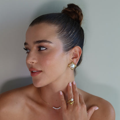 Woman wearing gold plated earrings CLAM and the waterproof gold plated ring SOLARA against a neutral background